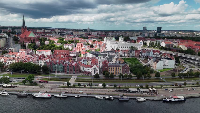 A wide aerial shot capturing the historic architecture, red roofs, and riverfront of Szczecin, Poland under a cloudy sky.