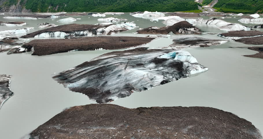 Huge blocks of ice stick out from the river. Green rocky shores at backdrop. Alaska wilderness.