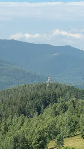 Vertical panning shot of mountain ridge with cell tower, trail, and valley view on summer day