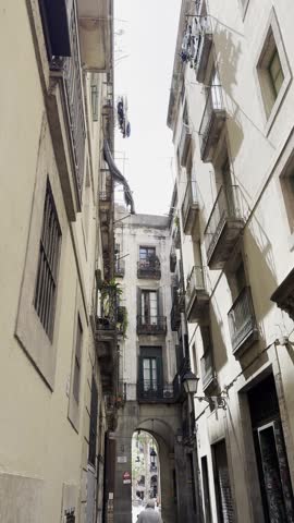 Looking up at historic apartment buildings and balconies lining a narrow street in Barcelona