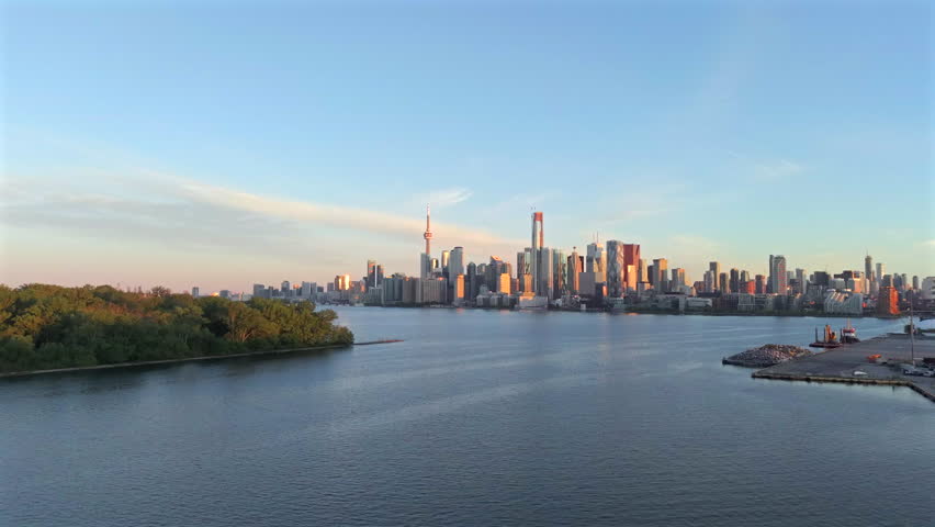 Climbing aerial drone video at dawn over Toronto Islands and Lake Ontario with downtown Toronto highrise skyline in warm sunrise light.