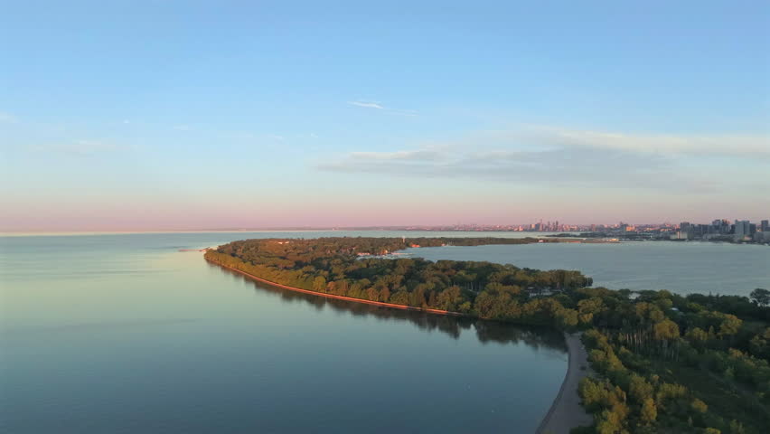 Rotating reveal aerial drone video at dawn over Toronto Islands with Lake Ontario and the downtown Toronto highrise skyline in the distance.