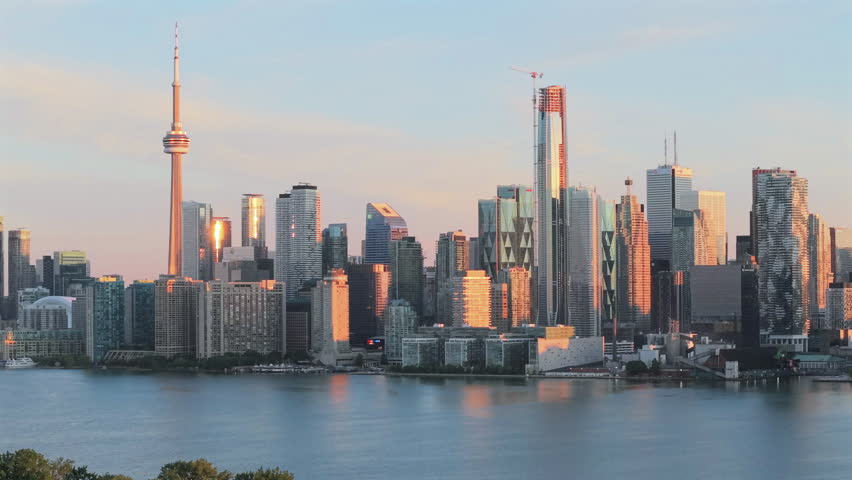 Slow zoomed panning aerial drone video of downtown Toronto highrise skyline at sunrise across Lake Ontario.