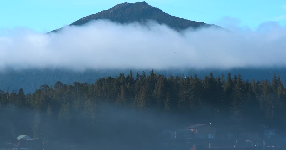 Fast moving clouds over pine forest with mountain backdrop in Ketchikan, Alaska