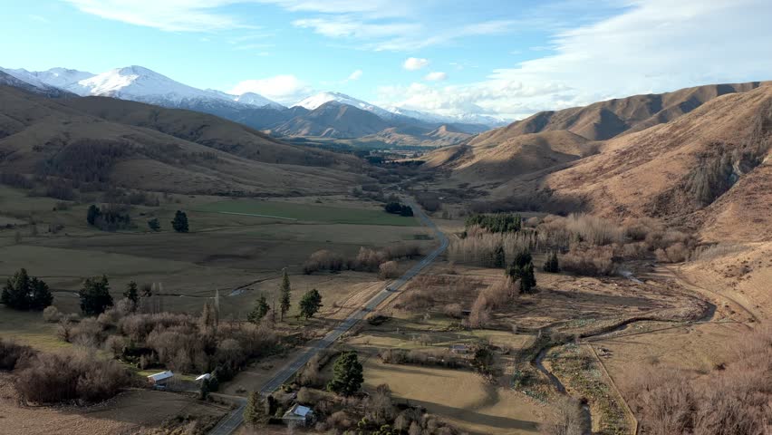 Aerial view of Burkes Pass with a road through a valley surrounded by snow-capped mountains and rolling hills in Burkes Pass, Canterbury Region, New Zealand.