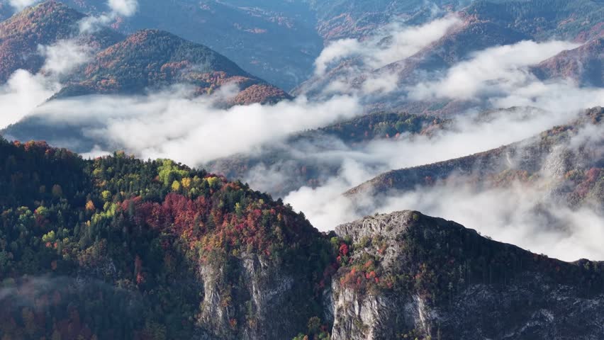 A dramatic mountain landscape in autumn, featuring a sea of clouds and thick fog flowing through the gaps in the valleys.