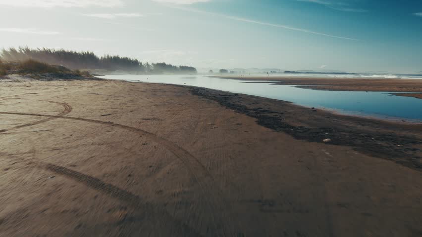 Fast flight forward on a low altitude over the sandy beach with lake with some birds. Coast of the Atlantic Ocean in Brazil