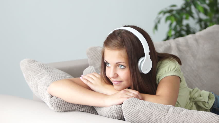 Sweet girl resting on couch and listening to music with smile
