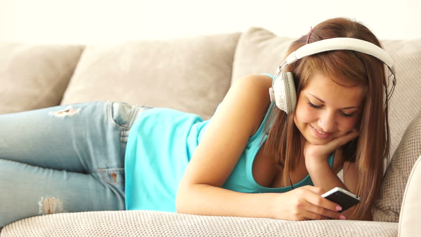 Young woman lying on couch with phone and listening to music
