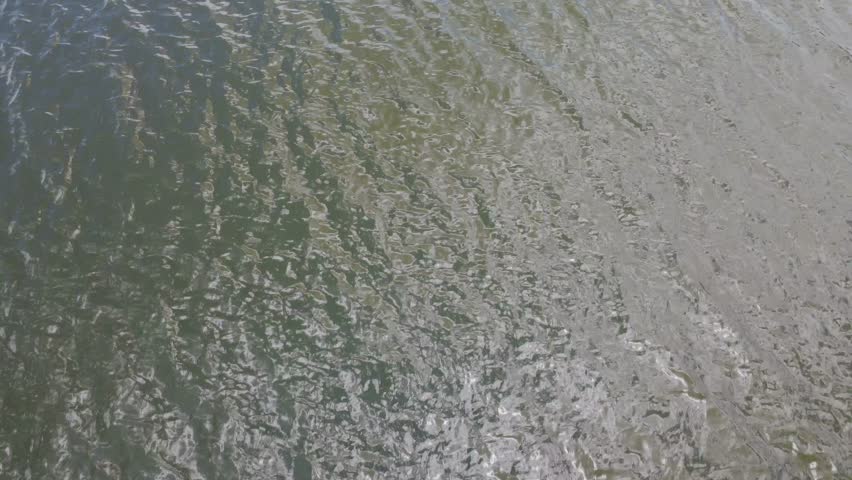 Drone rises from close water texture to a wide mountain lake landscape.