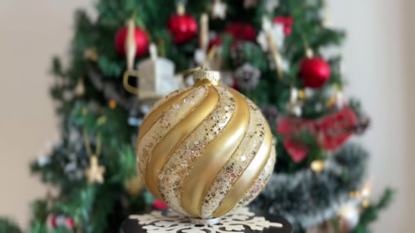 Golden Christmas bauble rotating with blurred tree