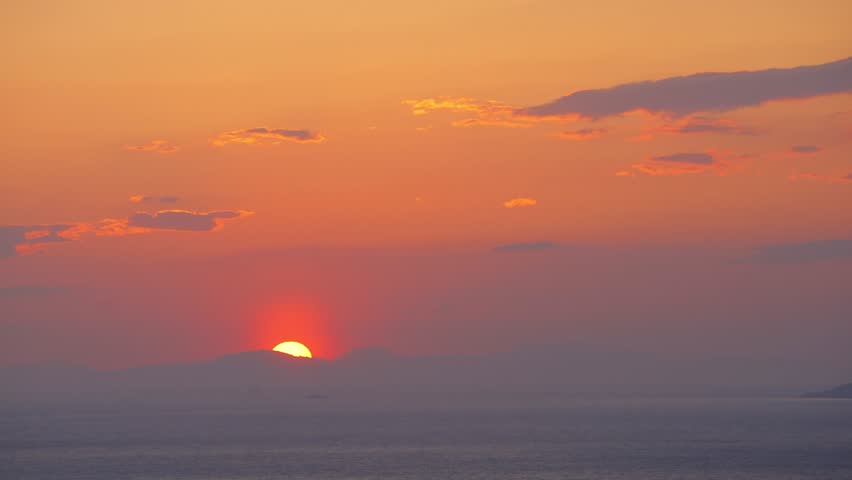Sunset with orange colors with sun setting behind the mountains and reflecting on the sea
