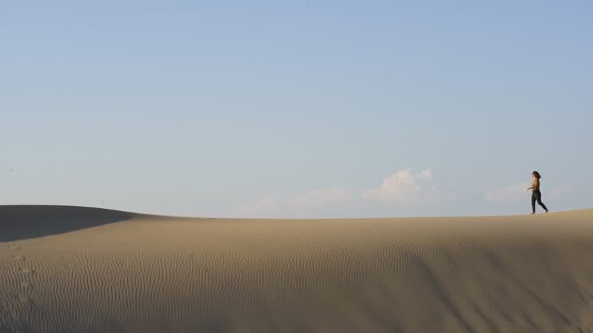 Young woman walking on sand dune in the desert enjoying freedom and adventure in Patara beach, Turkey in slow motion