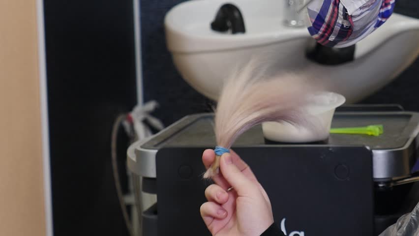 Client hand holding freshly cut long blonde hair strand, swinging it gently. Sad goodbye to long locks before major haircut and new color treatment in salon. Beauty salon concept. 4k video