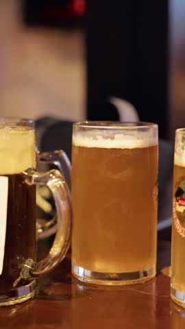 Glasses of beer on dark bar counter with foamy heads, amber color, and warm pub lighting