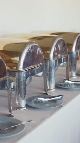 Elegant buffet table with stainless steel chafing dishes and serving tongs in banquet setting