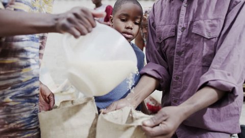 A mother and father from a poor African community work together with their young son, measuring out quantities of rice or grain. In slow motion.