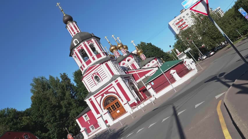 Traditional Russian Orthodox church featuring red walls, white ornaments, and golden domes with a bell tower under a bright blue sky