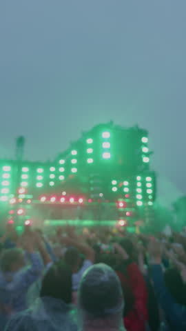 Blurred crowd watching outdoor concert stage with glowing green lights at dusk