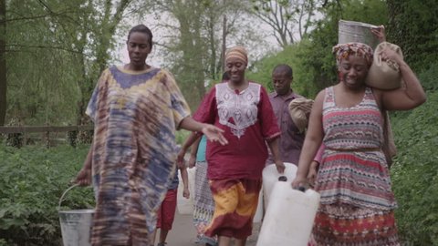 A family group of African villagers travel together with many containers, to find water to bring back to their village. In slow motion. Vídeo Stock