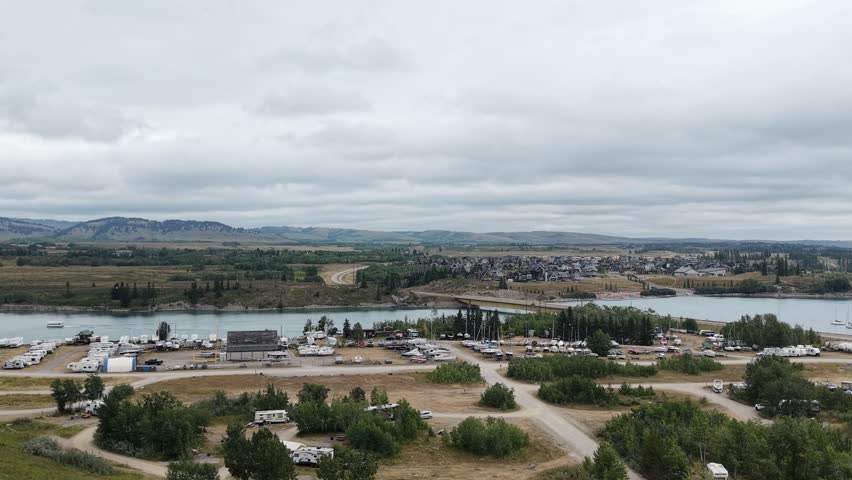 Aerial drone view of a lakeside recreation area surrounded by green landscape and a large body of water under a cloudy sky.