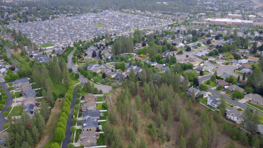 Aerial view of a tree-shaded Spokane, Washington neighborhood, with curving residential streets giving way to denser city development beyond.