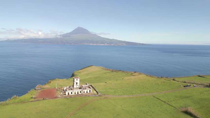 Cinematic aerial view, Lighthouse of Ribeirinha on Faial Island, Azores, Portugal, overlooking the Atlantic Ocean with Pico Mountain visible across the water