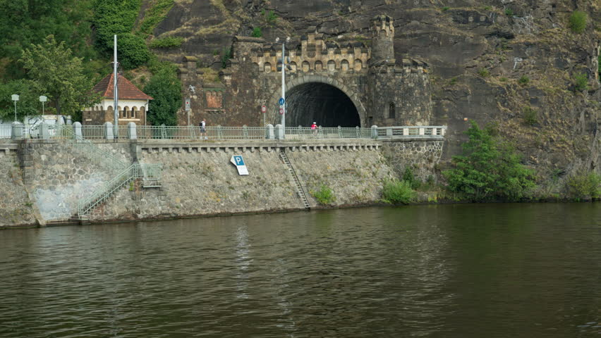 Historic Vysehrad stone tunnel portal stands built into a rocky cliff along Vltava River in Prague. The scenic embankment represents Czech travel destination and transport infrastructure.