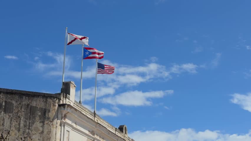 American and Puerto Rican flags waving in the breeze atop the historic fort stone walls in Old San Juan Puerto Rico under blue sky