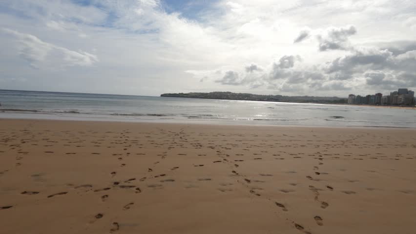 Playa de San Lorenzo beach with calm waves and cloudy sky in Gijon Spain, empty backdrop with footsteps in sand