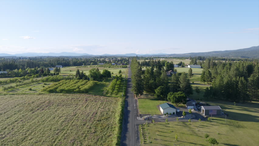 Aerial view of a straight rural road lined with trees, orchards, and farmhouses in the countryside near Spokane, WA.