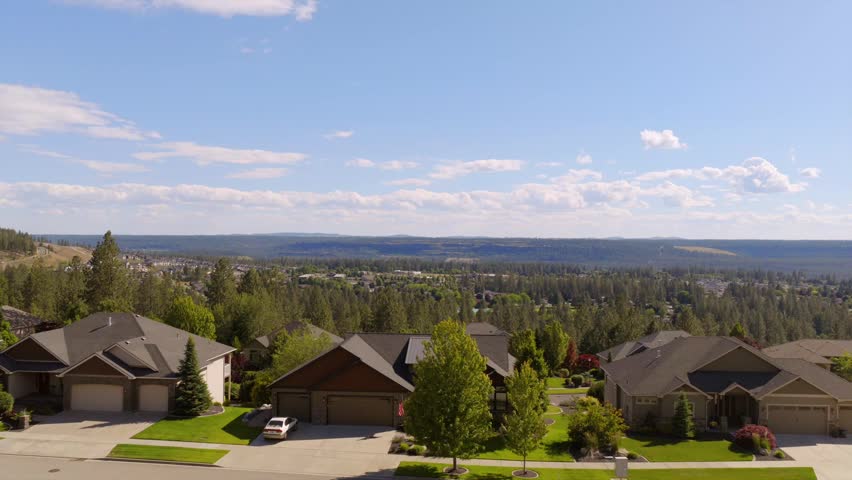 Aerial view from a hilltop neighborhood in Spokane, Washington, with large homes in the foreground and forested valley stretching to the horizon.