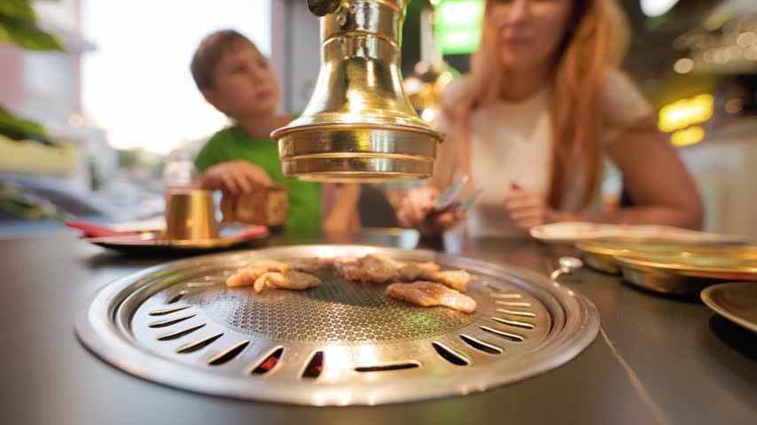 Family cooking meat at korean barbecue restaurant table