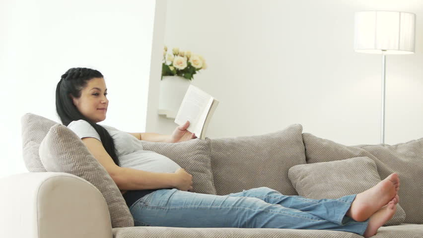 Pregnant woman resting on sofa reading book
