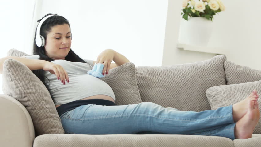 Pregnant woman listening to music and holding baby booties

