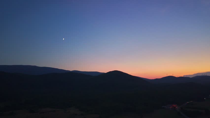 Aerial view of a crescent moon and sunset sky over silhouetted mountains in Croatia