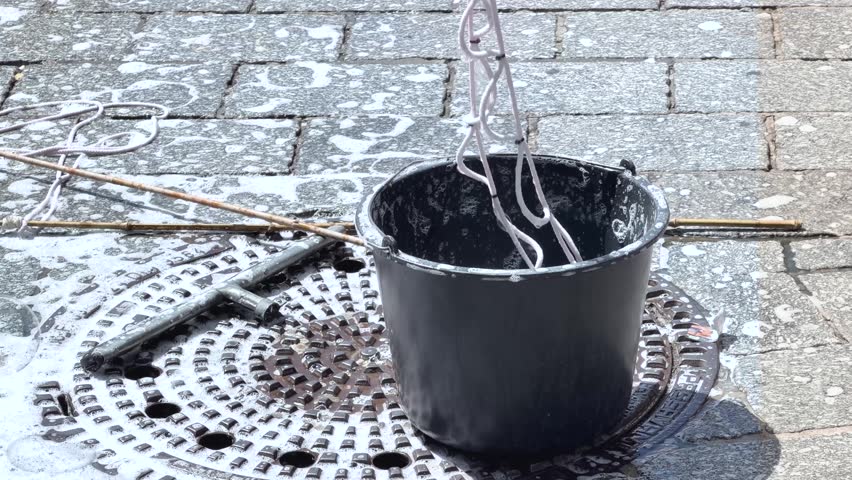 A bubble wand is lifted from a bucket of soapy water, creating large soap bubbles during an outdoor activity on a sunny day.