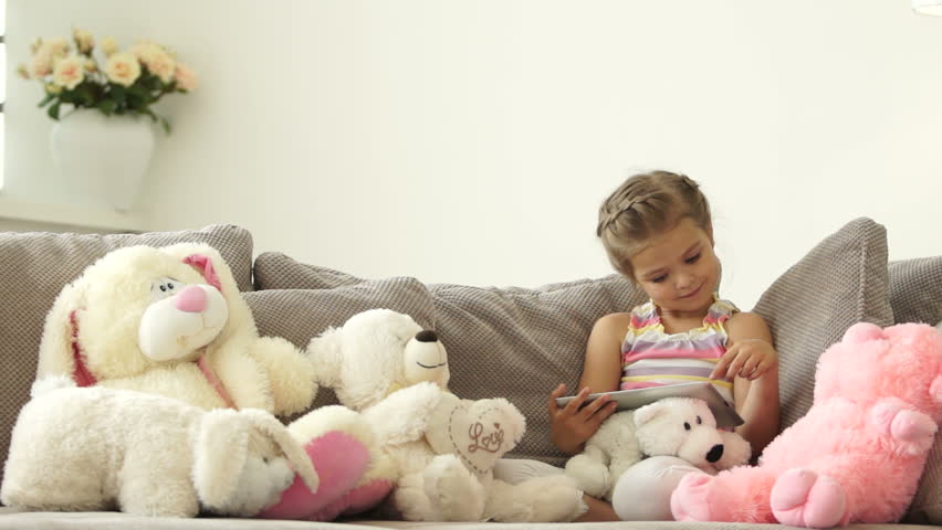 Little girl sitting on the couch with a tablet pc in toys
