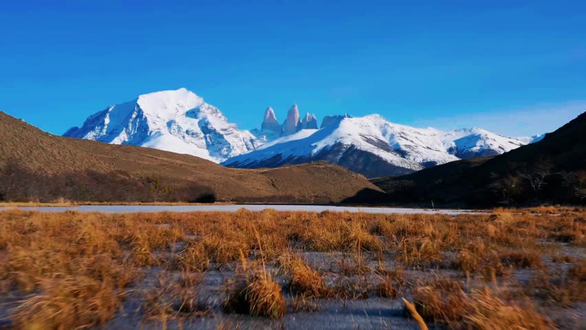 A breathtaking cinematic aerial view capturing the iconic snow-covered granite spires of Torres del Paine rising above an ice-flecked alpine lake.