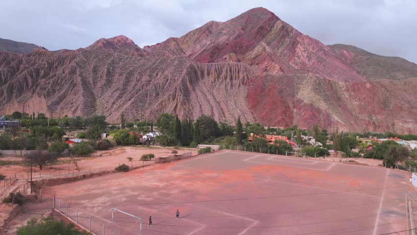 4K drone aerial view of a football field in Purmamarca, Jujuy, Argentina. A unique sports ground surrounded by the colorful Andean mountains and the iconic landscapes of the Quebrada de Humahuaca.