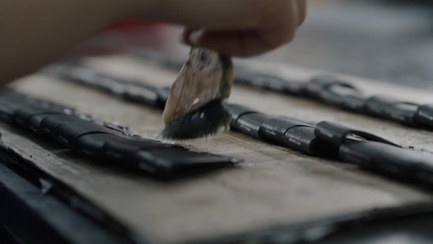 Worker applies adhesive to leather shoe parts on a workbench in a factory setting