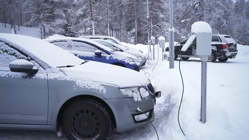 Snow covered cars plugged into electric heating posts for engine block heaters in outdoor parking lot during extreme cold winter weather