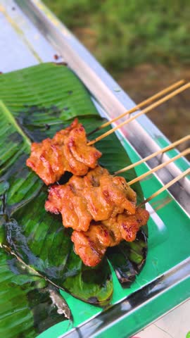 Close-up shot of freshly grilled pork skewers (Moo Ping) served on a fresh green banana leaf, highlighting the glossy marinade, smoky char marks, and authentic Thai street food culture.
