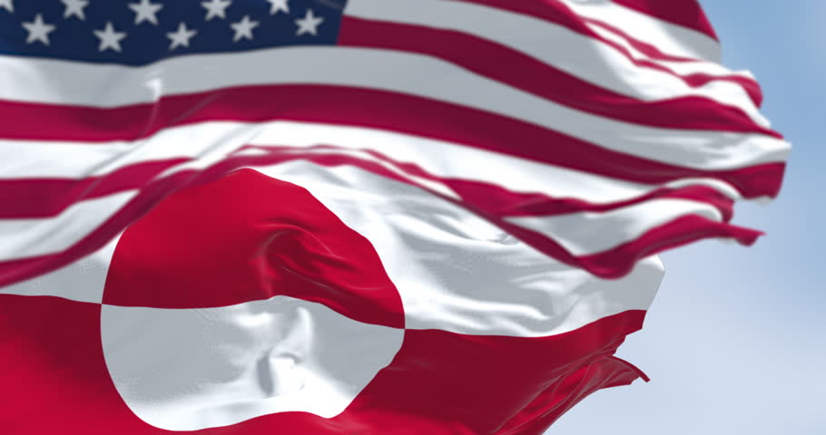 Flags of Greenland and the US waving in the wind on a clear day. Greenland is the world
