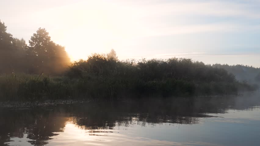 Beautiful early morning sunrise over calm river with gentle mist rising from water and lush green banks. Creating a peaceful and serene natural landscape with perfect reflections