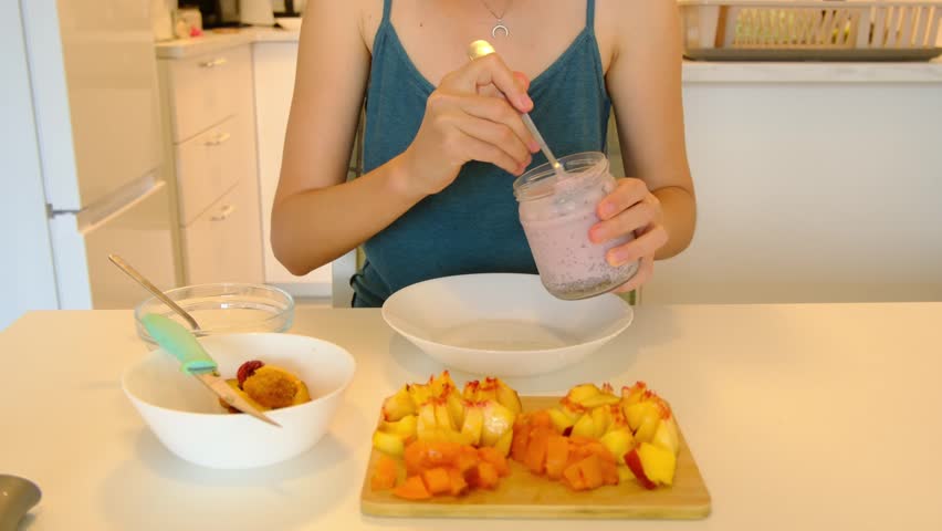 Young woman prepare tasty chia seed pudding with peaches and apricots at table, healthy eating habits