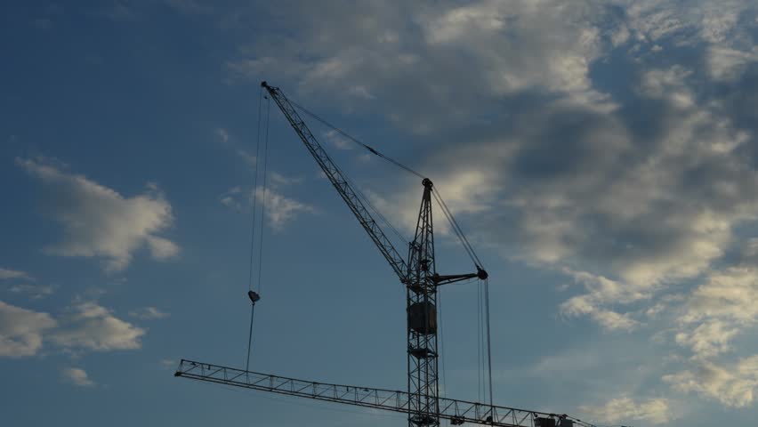 A tall construction crane stands against a cloudy blue sky.