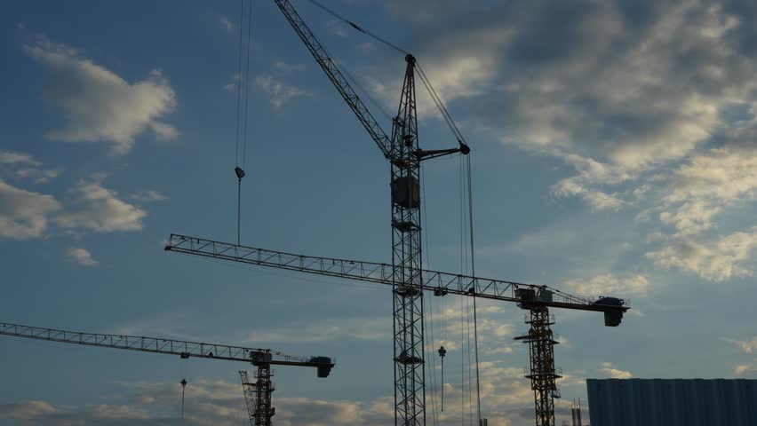 A tall construction crane stands against a cloudy blue sky.