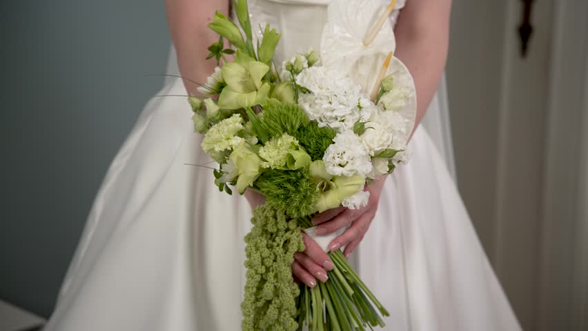 Close-up of a bride in a white wedding dress holding a modern bridal bouquet with green and white flowers.