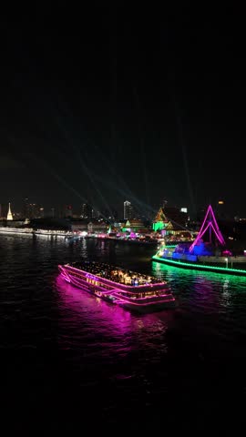 Colorful illuminated party boats sailing on the Chao Phraya River in Bangkok, Thailand at night with the city skyline in the background, offering a scenic dinner cruise for tourists.